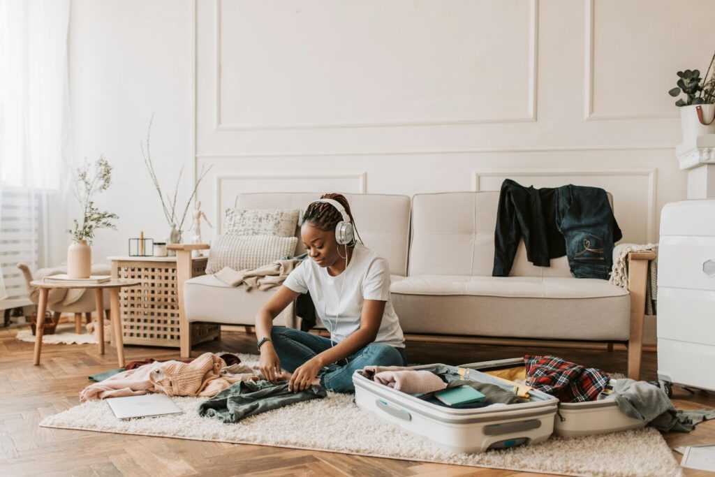 A woman wearing headphones packs a suitcase in a stylish living room, preparing for travel.