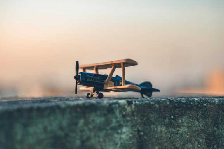 A vintage toy airplane sitting on a concrete surface against a warm sunset sky.