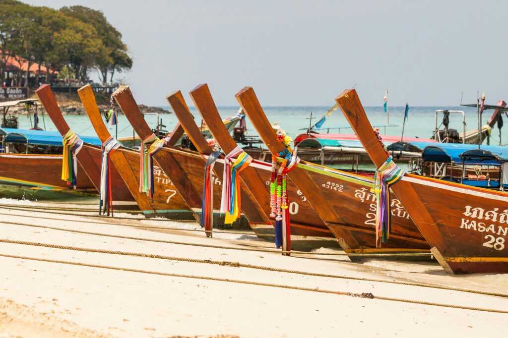 Vibrant longtail boats lined up on a sandy beach, perfect for travel and tourism imagery.